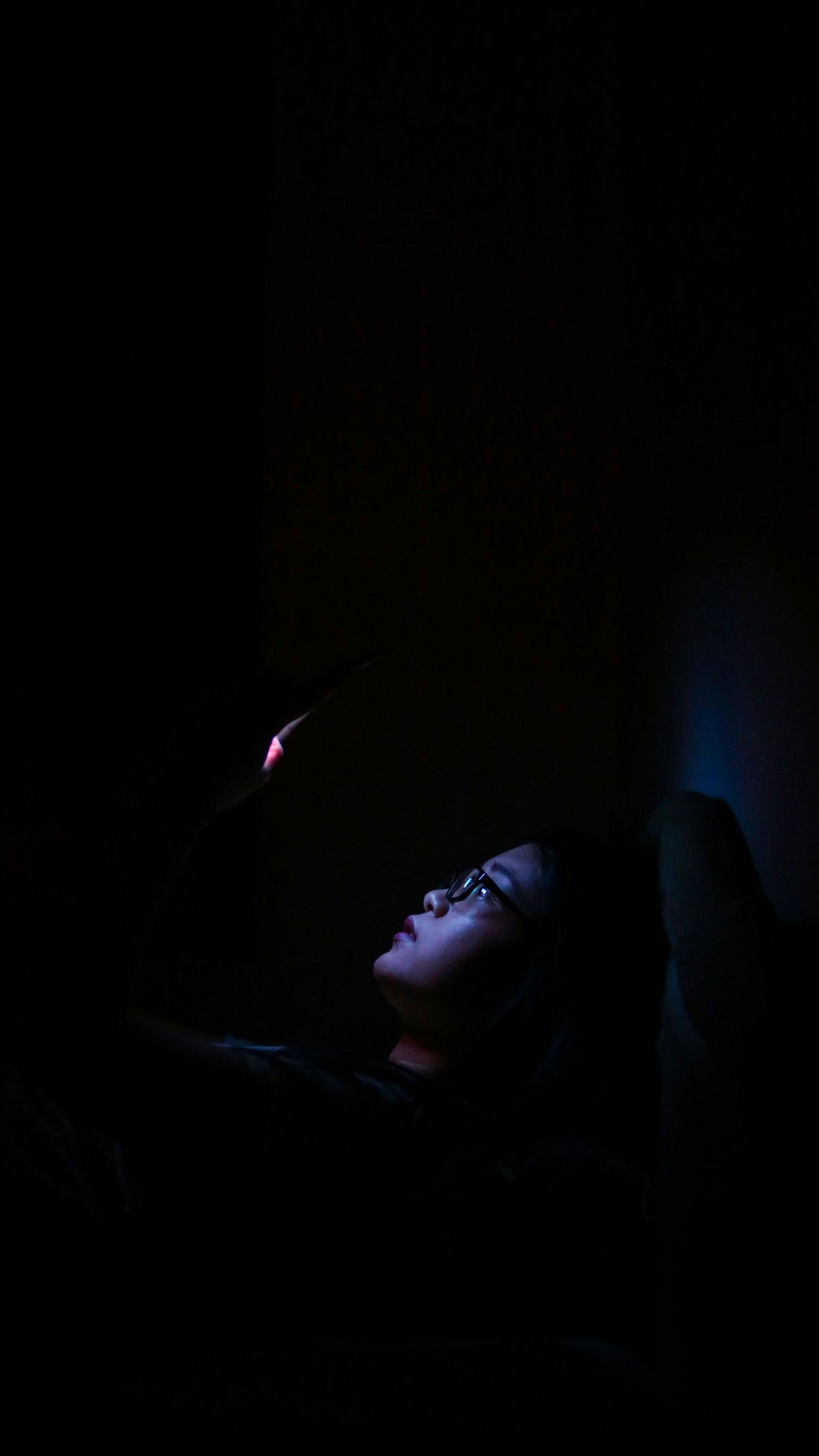 Persona iluminada por la luz del móvil en la oscuridad de la cama